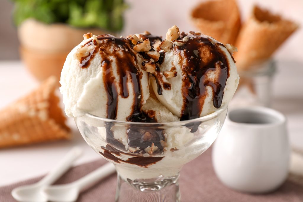 Tasty ice cream with chocolate topping and nuts in glass dessert bowl on table closeup